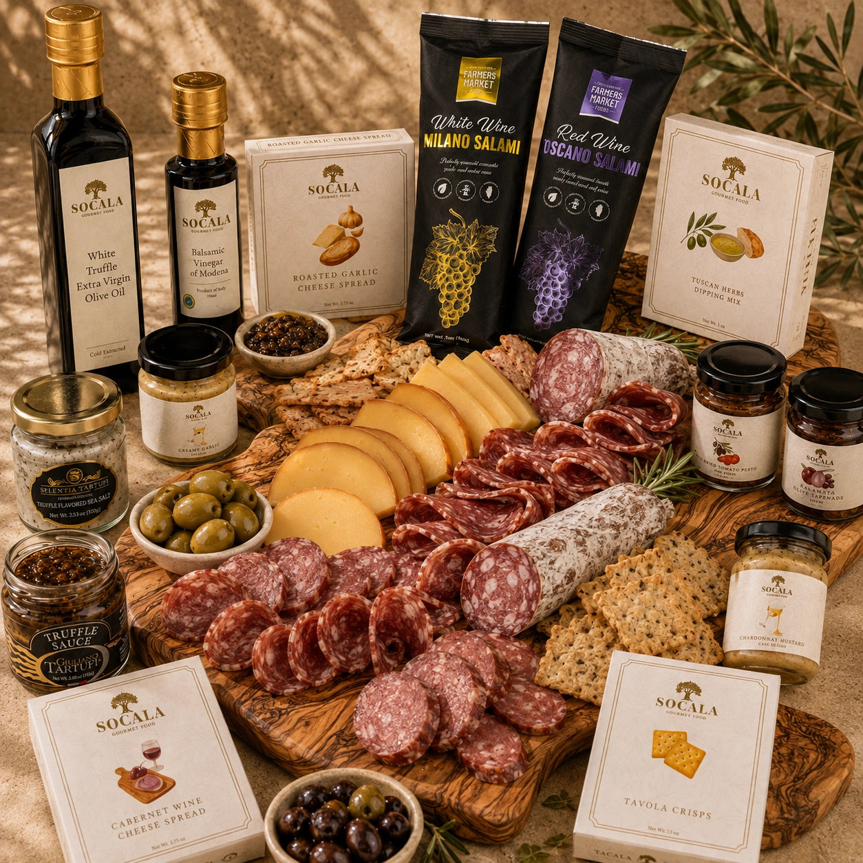 A styled charcuterie and cheese spread arranged on a wooden board with olive oil bottles, SOCALA cheese and crackers, salami, prosciutto, olives, nuts, and jars on a beige stone backdrop.