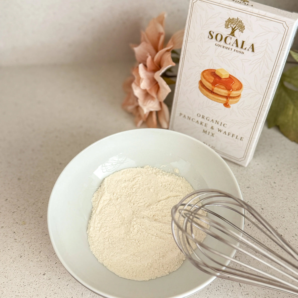 Socala Organic Pancake & Waffle Mix packaging with a bowl of flour and whisk on a light surface.