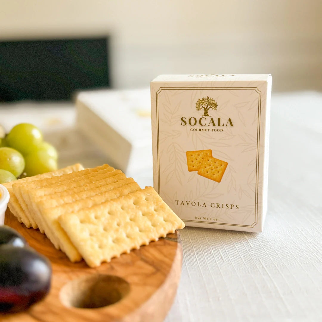 Box of Socala Tavola Crisps with crackers on a wooden board and grapes in the background